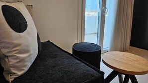 A modern room with a dark grey sofa, a round wooden table, and a black ottoman. - Aristotle Suites, Althea

 (Adamantas)