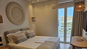 A bedroom with a large bed, a small table, a hanging light, and a view of the outdoors through a sliding door. - Aristotle Suites, Althea

 (Adamantas)