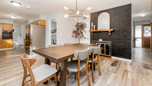 A modern kitchen with a wooden dining table and chairs, a black brick accent wall, and a hanging light fixture. - Charming 3-bedroom house in peaceful neighborhood  (Bloomington)