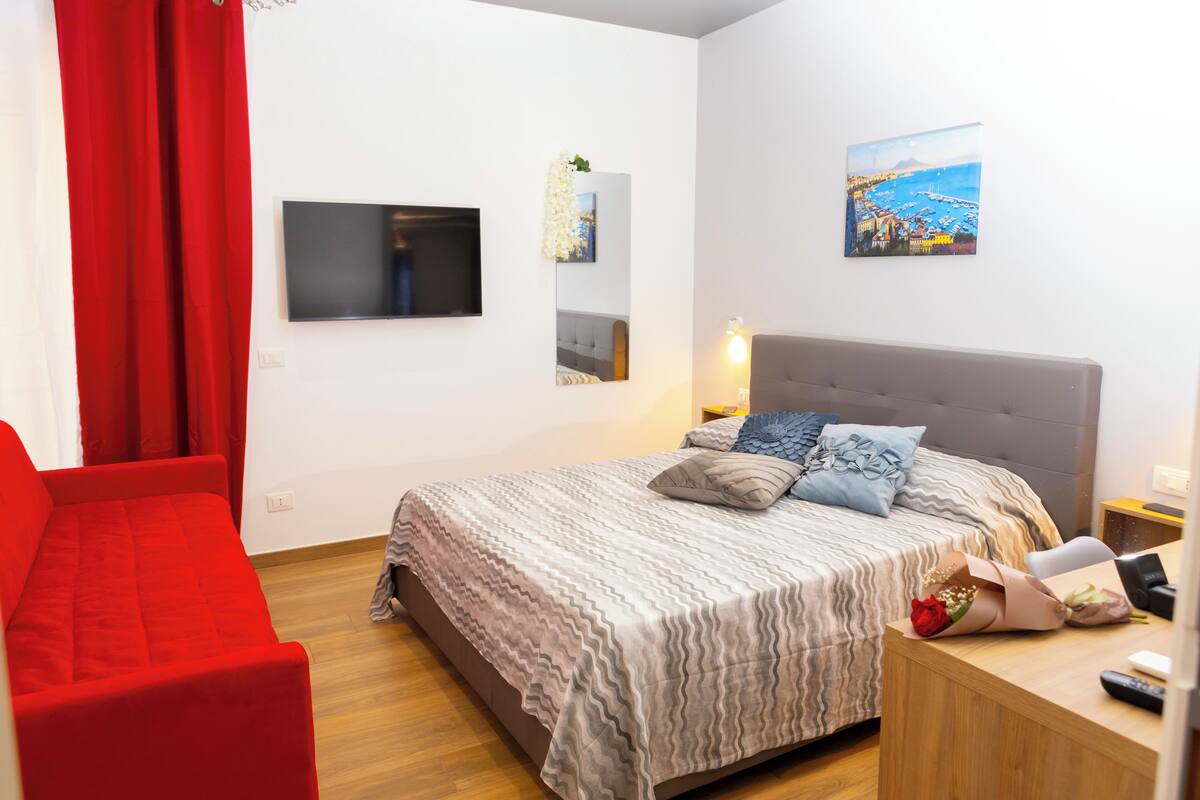 A modern bedroom with a bed, a red chair, a TV, and a painting on the wall.