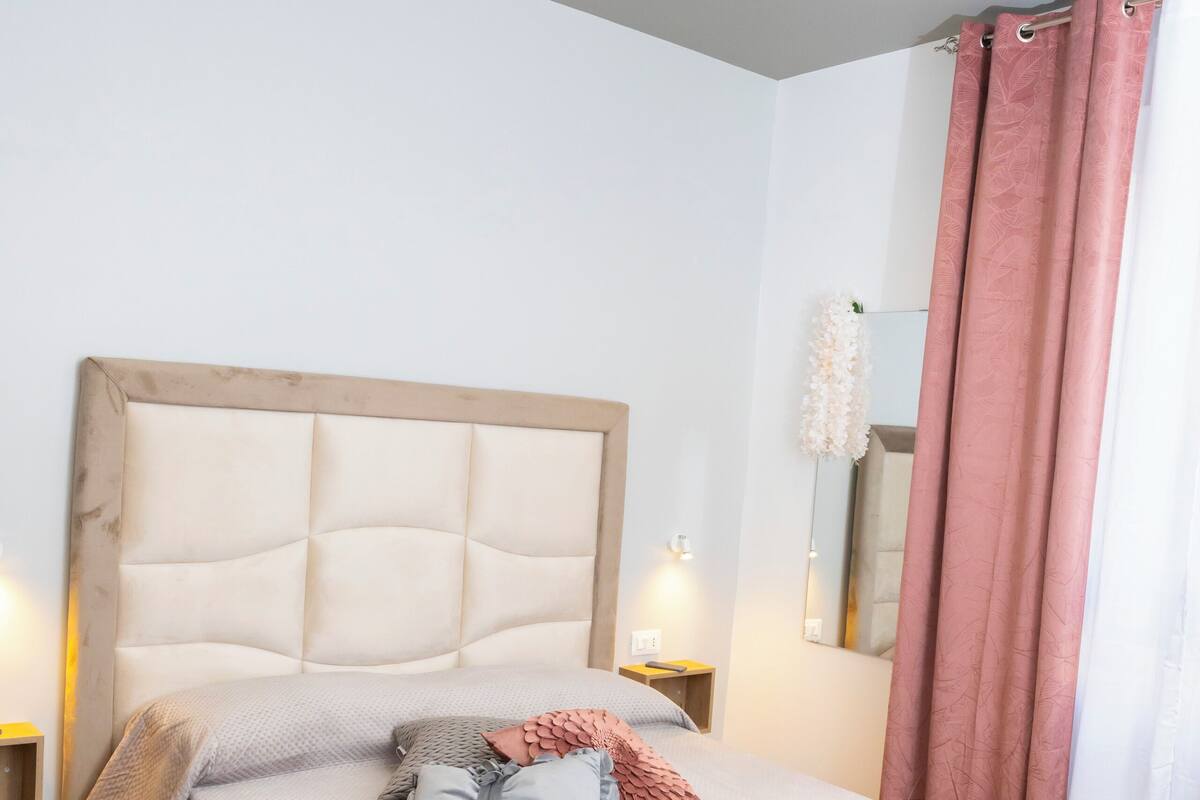A neatly made bed with a headboard, two bedside tables with lamps, and a large mirror on the wall.
