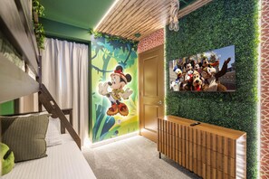 A room with a bunk bed, a mural of Mickey Mouse, a TV on the wall, and a green wall with a giraffe pattern.