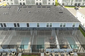 A modern building with a flat roof, large windows, and a swimming pool area with multiple air conditioning units.