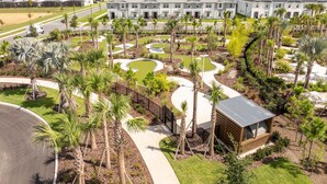A residential area with modern buildings, a landscaped garden with palm trees, and a small wooden structure. - 1268- Great 5 Bedroom Home, Pool & Game Room (Clermont)