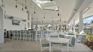 A covered outdoor seating area with white tables and chairs, a bar, and a view of palm trees. - 1268- Great 5 Bedroom Home, Pool & Game Room (Clermont)