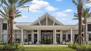 A modern hotel with a symmetrical facade, a central entrance with a glass door, and palm trees framing the entrance. - 1268- Great 5 Bedroom Home, Pool & Game Room (Clermont)