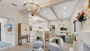 A spacious living area with a modern chandelier, a painting on the wall, and a cozy seating arrangement.