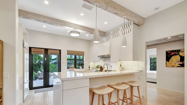 A modern kitchen with a large island, bar stools, and a view of the outdoor patio.