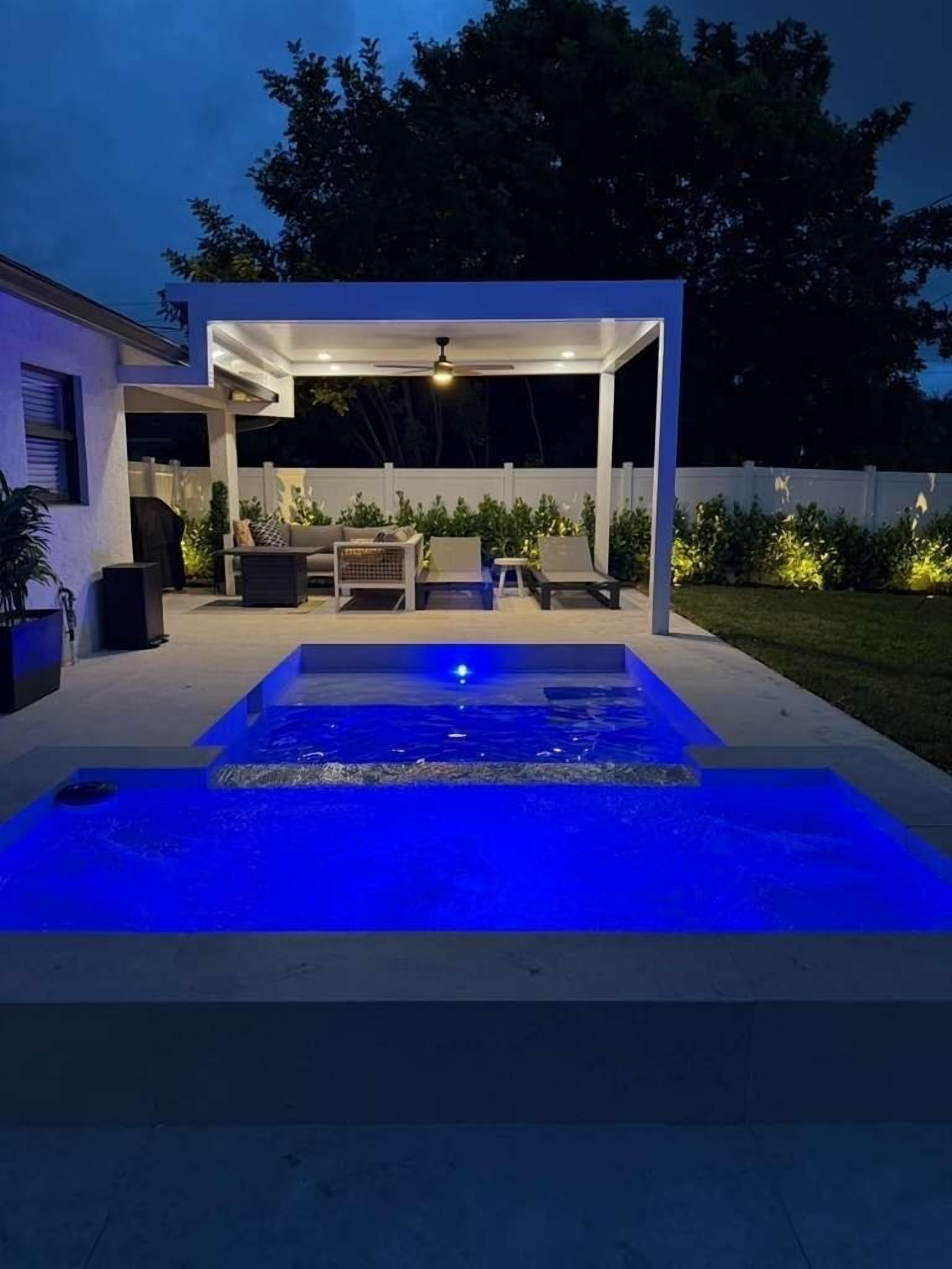 Een modern buitenzwembad met een overdekte zithoek en een verlichte waterattractie.