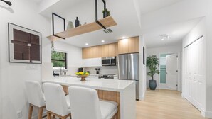 A modern kitchen with a central island, bar stools, stainless steel appliances, and wooden cabinets. - Casa Calma
2 min to Famous Atlantic Ave, Pool coming Oct 2025 (Delray Beach)