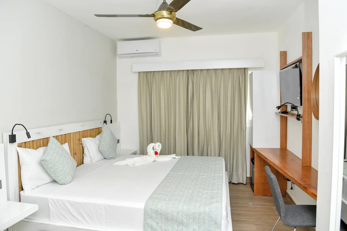 A hotel room with a bed, a desk, a chair, a ceiling fan, and a TV.