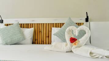 Una cama con cabecera de bambú, dos almohadas y una toalla dispuesta en forma de corazón con una rosa.