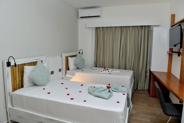A hotel room with two single beds, a desk, a chair, an air conditioning unit, and a curtain.