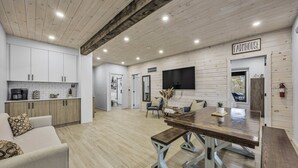 Uma sala ampla com teto de madeira, uma mesa de jantar e uma cozinha com armários brancos.