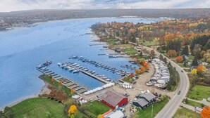 An aerial view of a marina with boats docked, surrounded by autumn-colored trees and residential buildings.