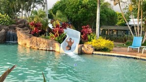 A pool with a waterfall feature, surrounded by tropical plants and a lounge chair. - Kiahuna Paradise condo with A/C (Koloa)