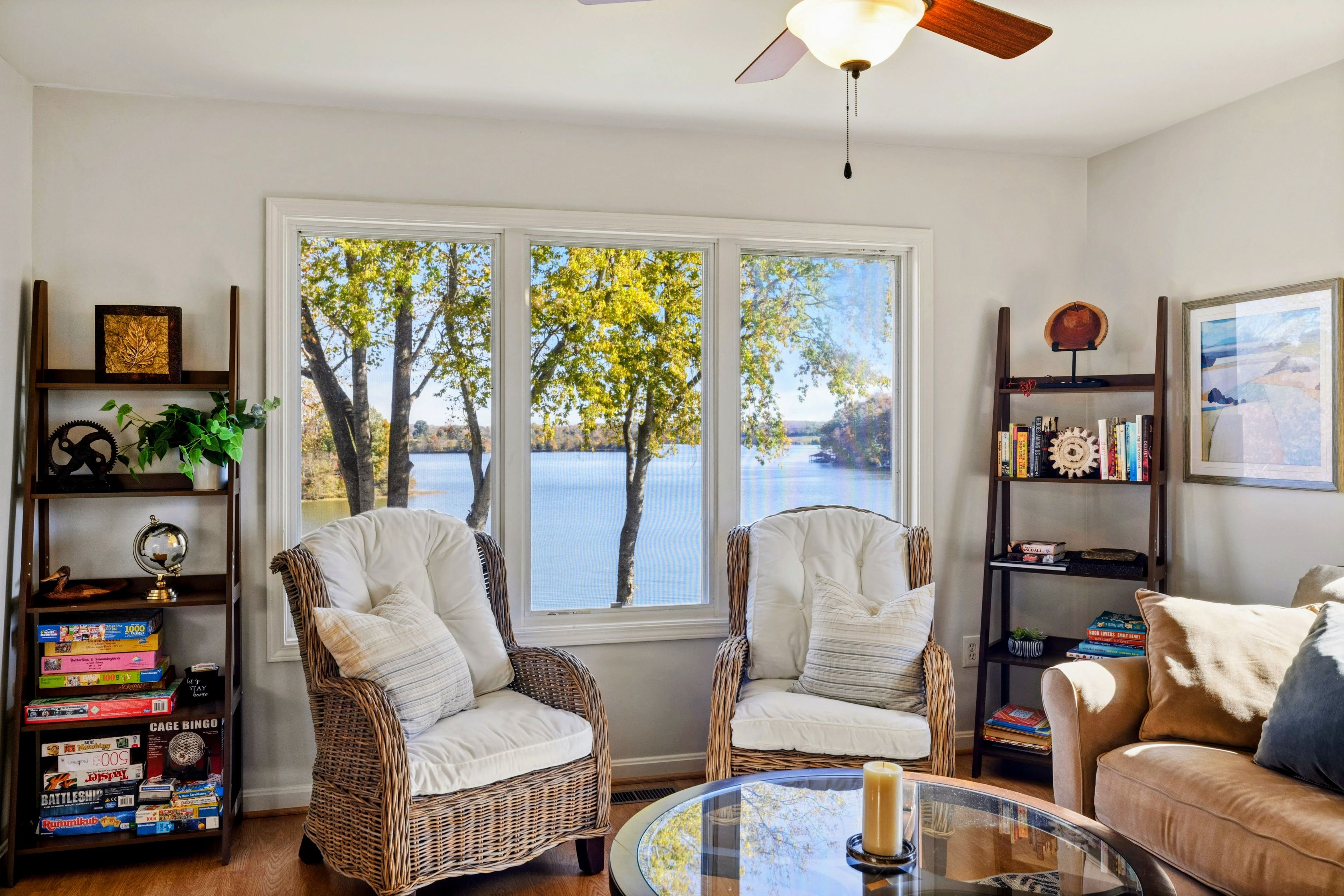 A room with two wicker chairs, a glass table, and a bookshelf with board games.