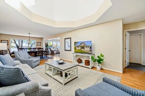 A spacious living room with a high ceiling, a dining area, and a view of a lake.