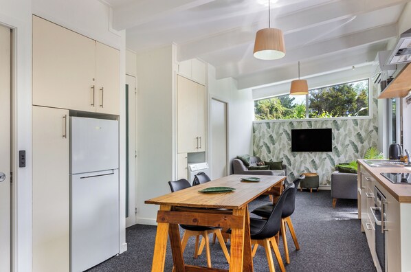 A modern kitchen with a dining area, a built-in TV, and a large window overlooking greenery.