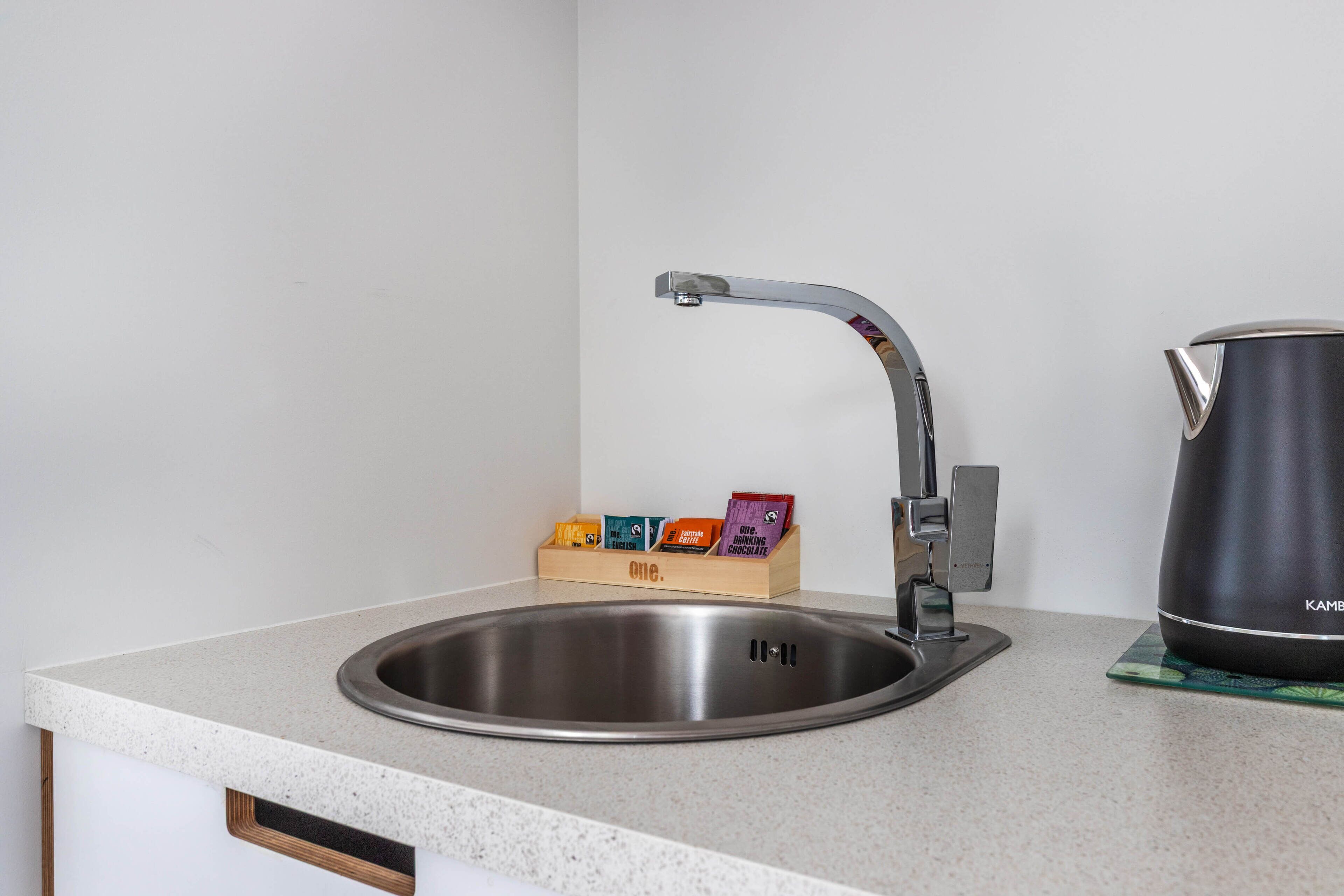 A kitchen with a stainless steel sink, a modern faucet, and a kettle on the counter.