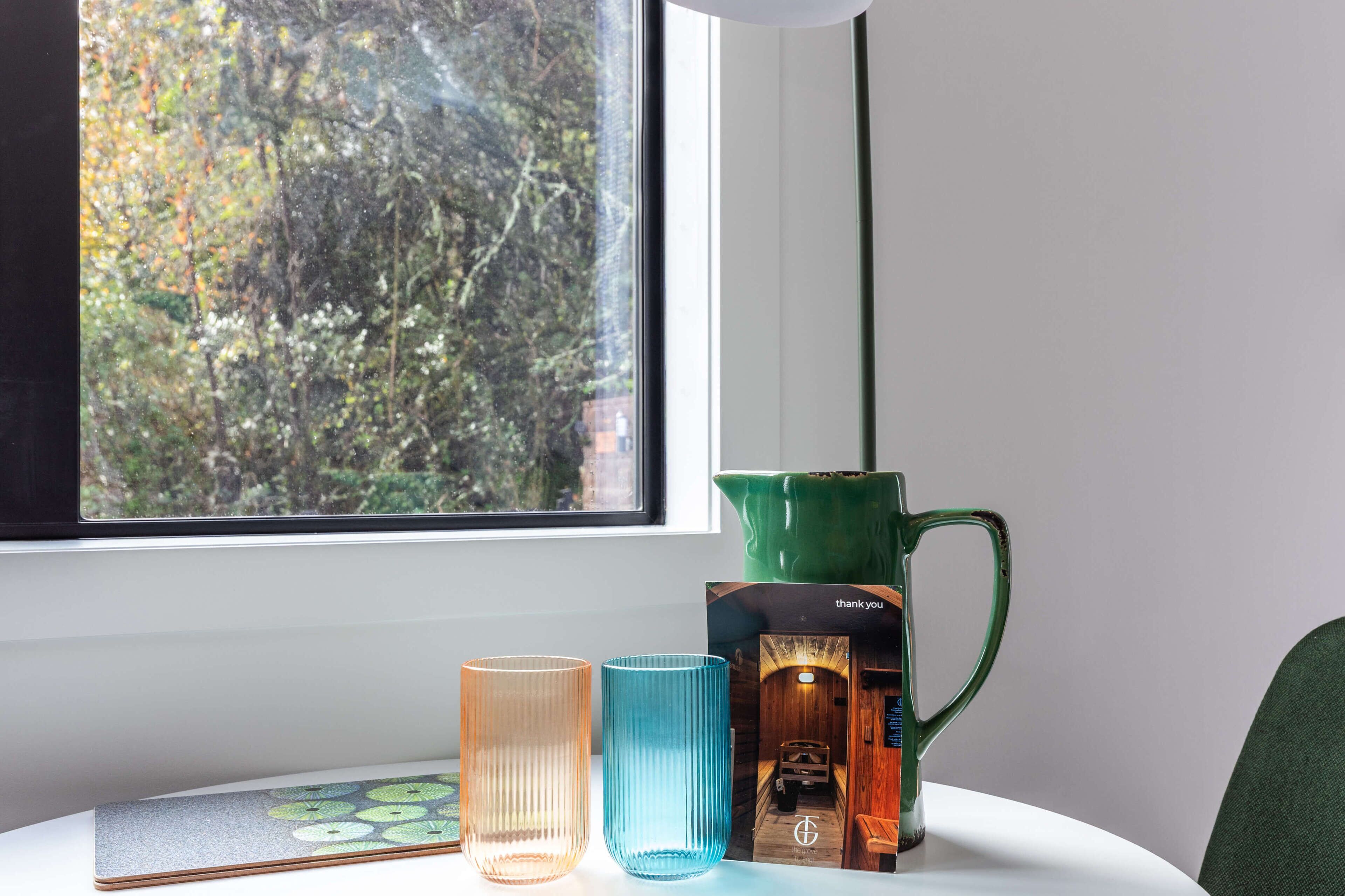Uma mesa com um jarro verde, dois recipientes de vidro e um cartão de agradecimento.