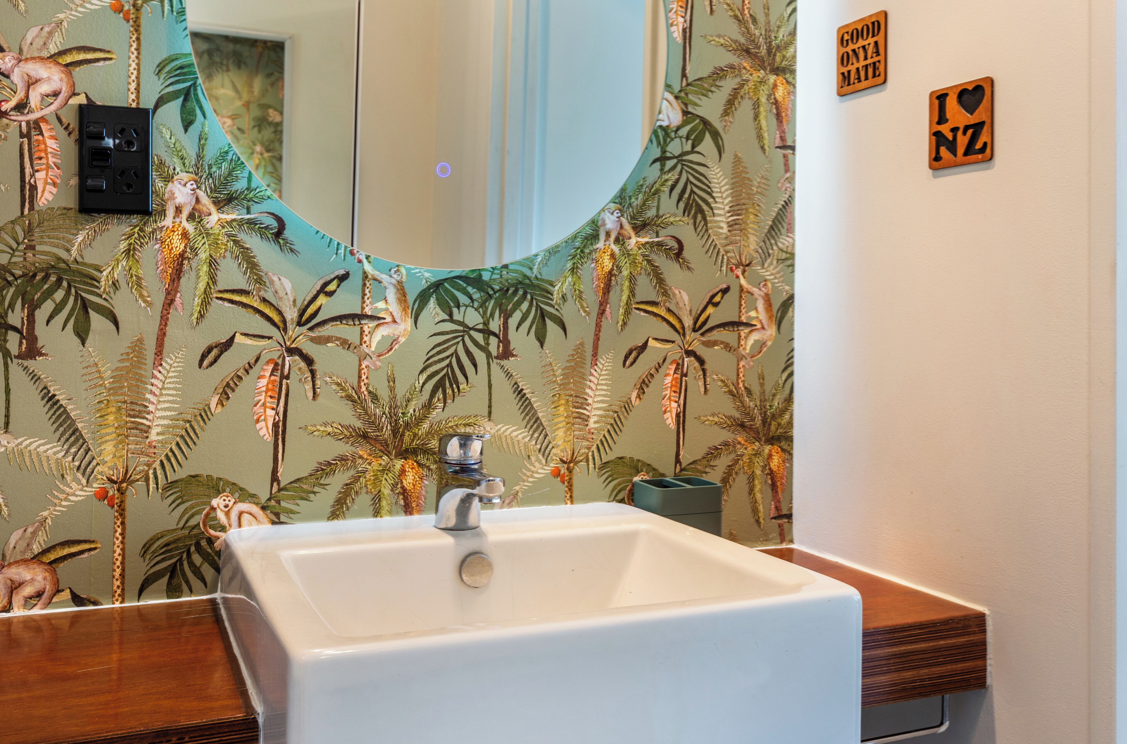 Een badkamer met een wit wastafelmeubel, een spiegel en een muur met tropisch behang.