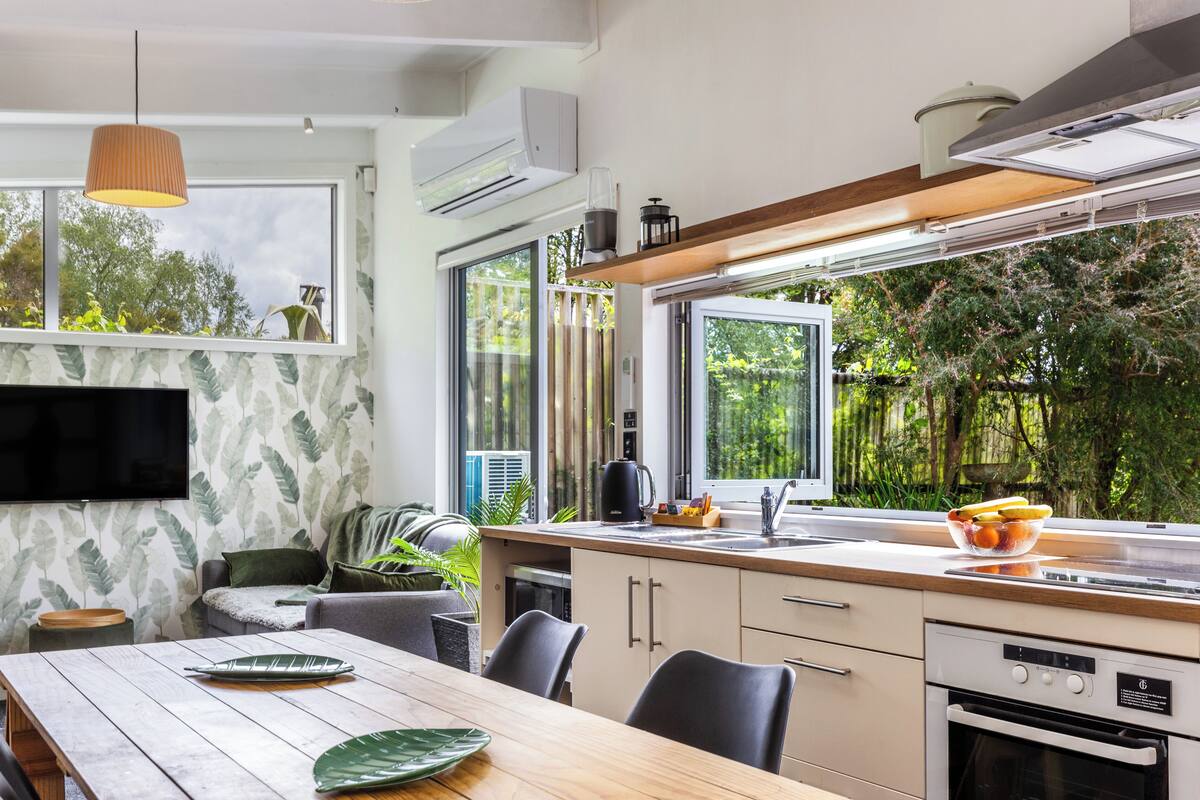 A modern kitchen with a large window, a dining area with a wooden table, and a built-in oven.