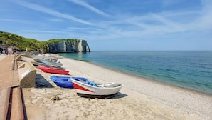 Una playa con barcos alineados en la orilla, un acantilado con un arco natural y un cielo azul despejado.