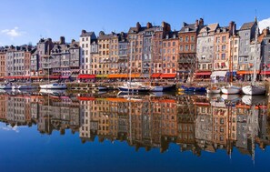 Un muelle con edificios históricos, un puerto deportivo con barcos y un reflejo claro en el agua.