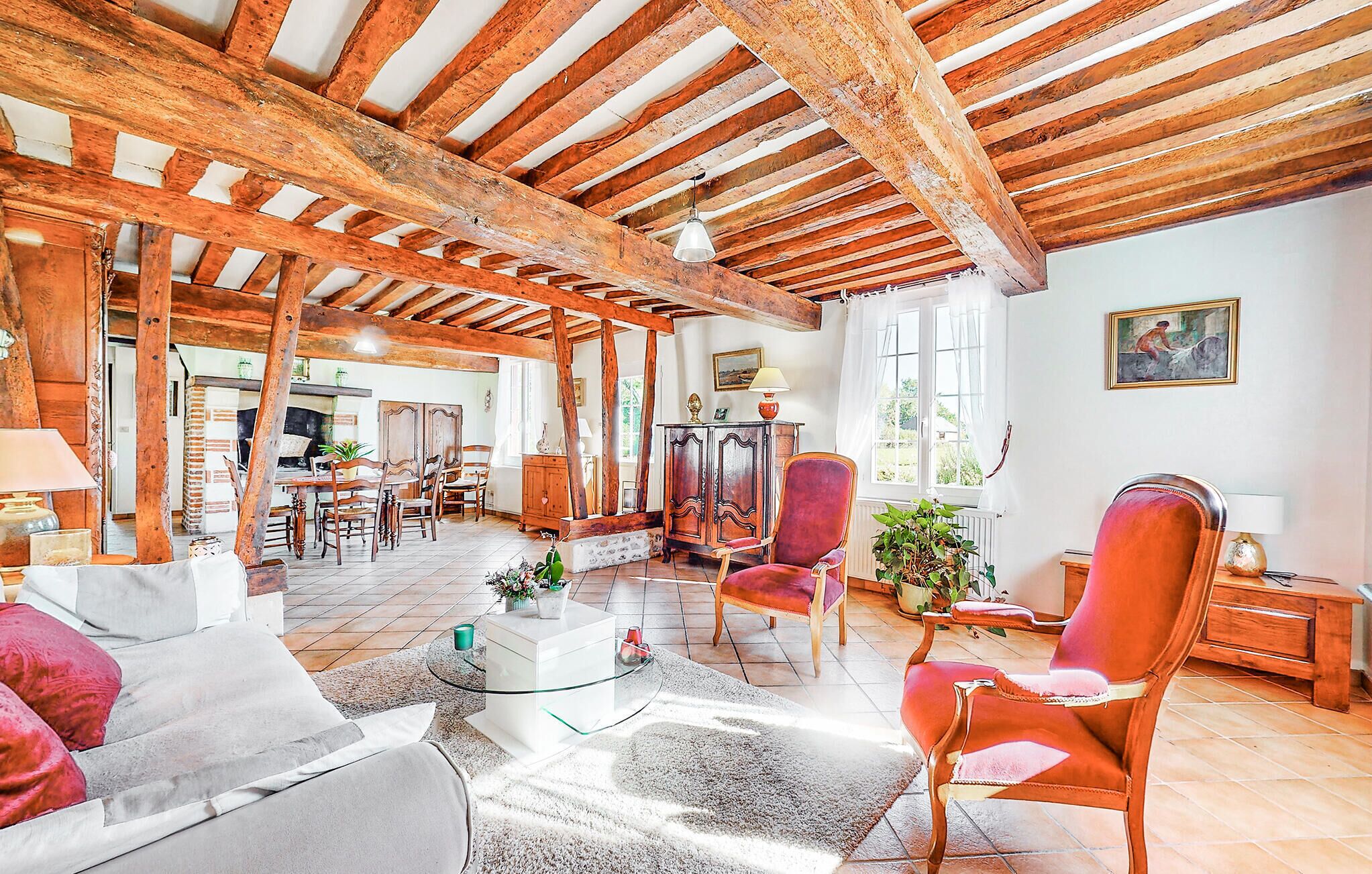 Une pièce rustique avec des poutres apparentes, un coin repas avec des meubles en bois et un espace salon confortable avec des fauteuils rouges et une table basse en verre.