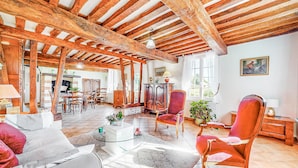 Una habitación rústica con vigas de madera a la vista, una zona de comedor con muebles de madera y una acogedora sala de estar con sillas rojas y una mesa de centro de vidrio.