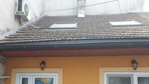 A building with a tiled roof, two windows with white frames, and a mural on one window. - Hidden place in pedestrian zone (Novi Sad)