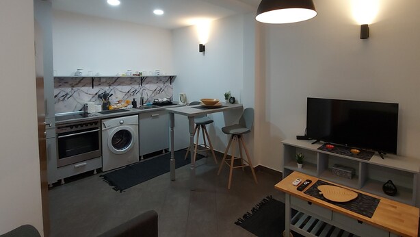 A modern kitchen with a built-in oven, a washing machine, and a dining area with a TV and a small table. - Hidden place in pedestrian zone (Novi Sad)