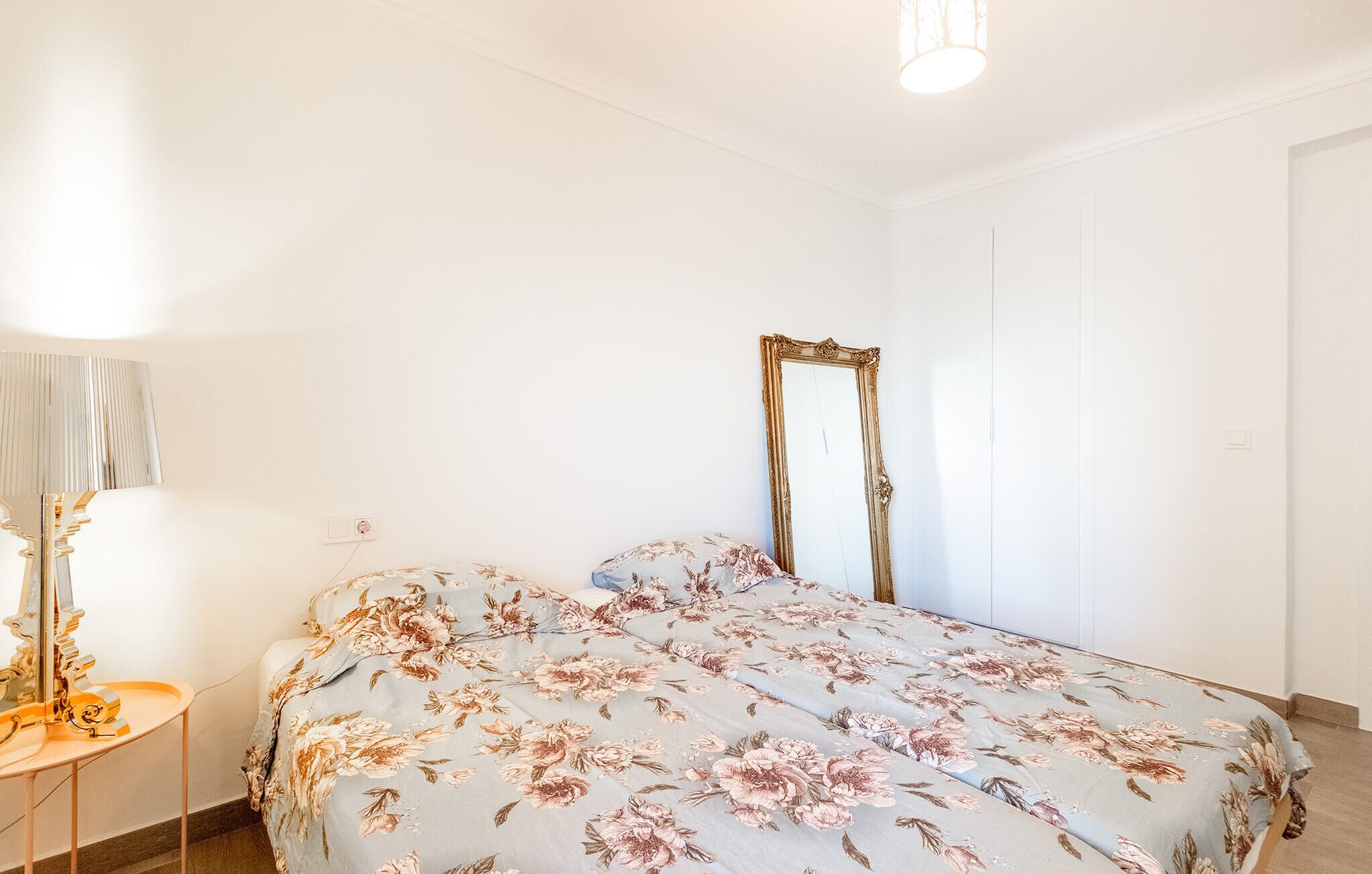 A bedroom with a bed, a mirror, a lamp, and a door.