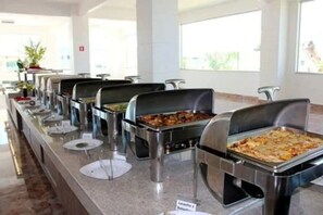 Un buffet proposant différents stands de nourriture, dont un stand à pizzas, installé dans un espace intérieur bien éclairé et doté de grandes fenêtres.