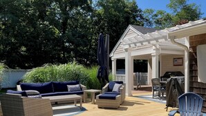 A covered outdoor deck with seating, a grill, and a pergola. - New Eastham Oceanside Guest Suite with Pool and Hot Tub (Eastham)