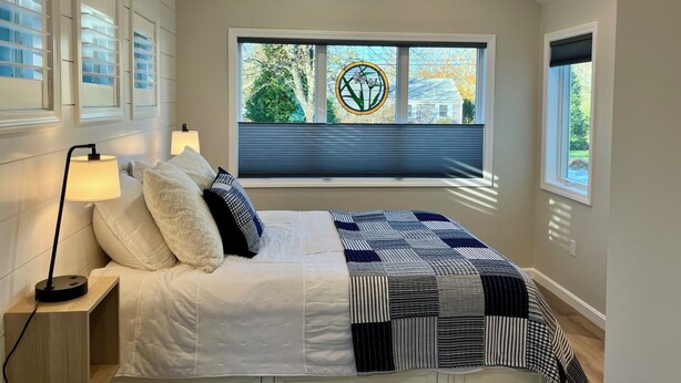A bedroom with a bed, bedside lamps, a window with blinds, and a ceiling fan. - New Eastham Oceanside Guest Suite with Pool and Hot Tub (Eastham)