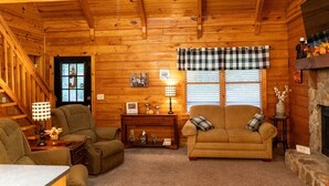 A cozy log cabin interior with a fireplace, wooden walls, a sofa, and a dining table. - Visit Star Haven for Labor Day - Fiber Wifi! - Close to Callway Gardens (Warm Springs)