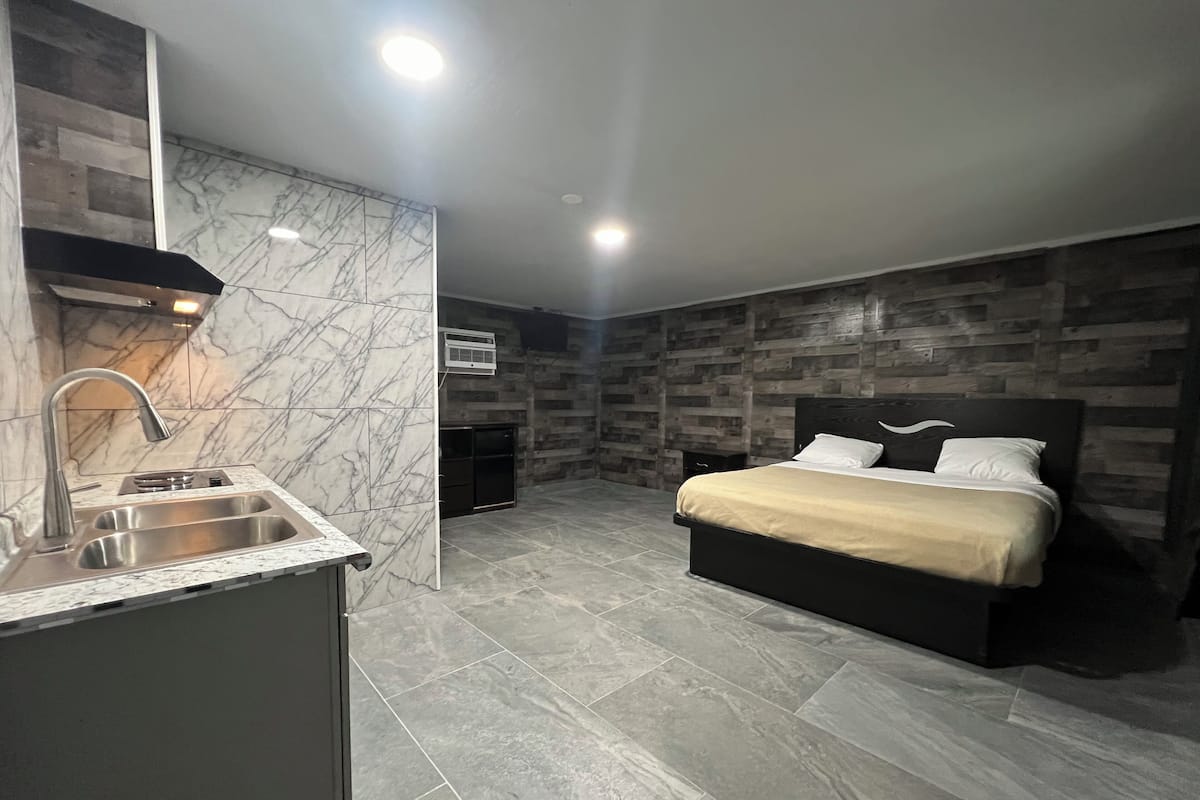 A modern bedroom with a large bed, a built-in nightstand, and a marble-tiled bathroom with a sink and vanity.