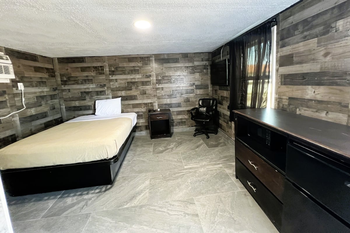 A bedroom with a bed, a desk, a chair, and a TV.