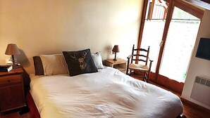Un dormitorio con una cama grande, una mesita de noche de madera, una silla y un ventanal con vistas al exterior.