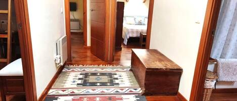 A hallway with wooden flooring, a bench, and a patterned rug.