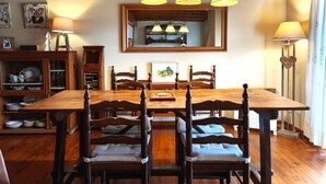 Un comedor con mesa y sillas de madera, iluminación colgante y un espejo sobre la mesa.