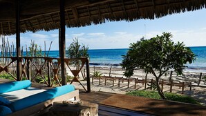 A wooden deck with a thatched roof overlooking a beach with a wooden fence and trees. - THE PALMS VILLA - Six Bedroom Villa, Sleeps 12 (South East Zanzibar)