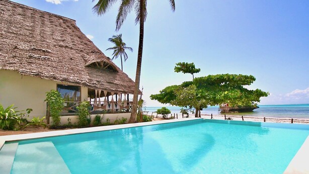 A clear blue pool with a thatched-roof building and palm trees. - THE PALMS VILLA - Six Bedroom Villa, Sleeps 12 (South East Zanzibar)