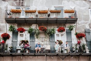 Un balcon orné de plantes et de fleurs en pot, avec une balustrade et la façade d’un immeuble.