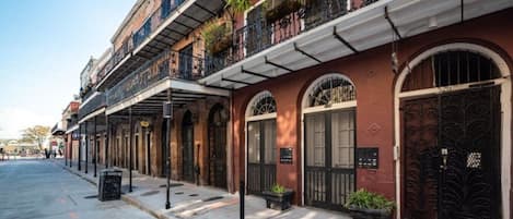 Una hilera de edificios históricos con ventanales arqueados y balcones, una acera y una calle.