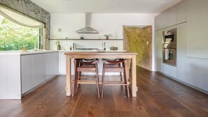 A modern kitchen with a central island, two wooden stools, a stainless steel range hood, and built-in appliances.