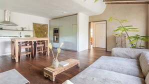 A modern living room with a wooden coffee table, a grey sofa, and a dining area with a wooden table and chairs.