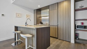 A modern kitchen with a central island, bar stools, a microwave, and a built-in oven. - The Pinnacle Carlton 69th Floor City Views (Carlton)